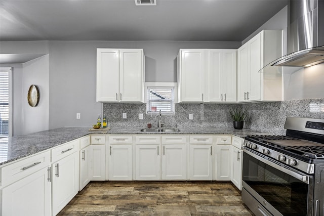 kitchen featuring a sink, light stone counters, white cabinetry, wall chimney range hood, and stainless steel gas range