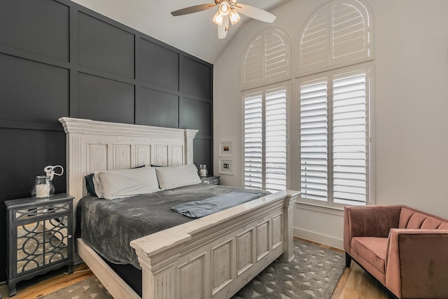 bedroom featuring vaulted ceiling, a decorative wall, wood finished floors, and baseboards