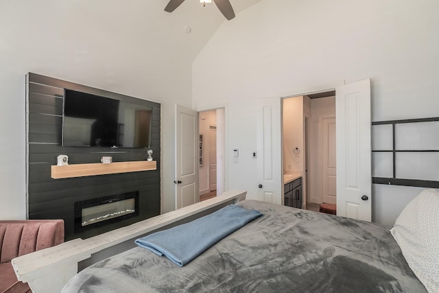 bedroom with high vaulted ceiling, a ceiling fan, a glass covered fireplace, and ensuite bathroom