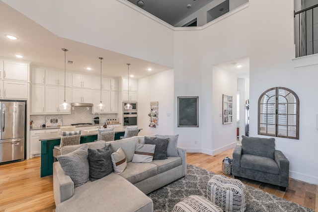 living area with light wood-style flooring, baseboards, and a towering ceiling