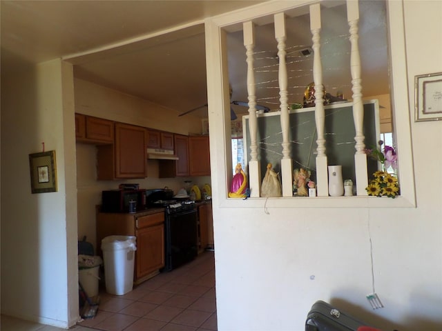 kitchen featuring under cabinet range hood, light tile patterned flooring, brown cabinets, and black range with gas stovetop