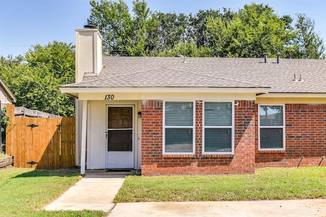 bungalow featuring fence, a front yard, a shingled roof, brick siding, and a chimney