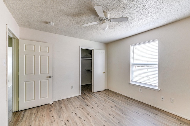 unfurnished bedroom featuring ceiling fan, a closet, a textured ceiling, a walk in closet, and light wood-type flooring