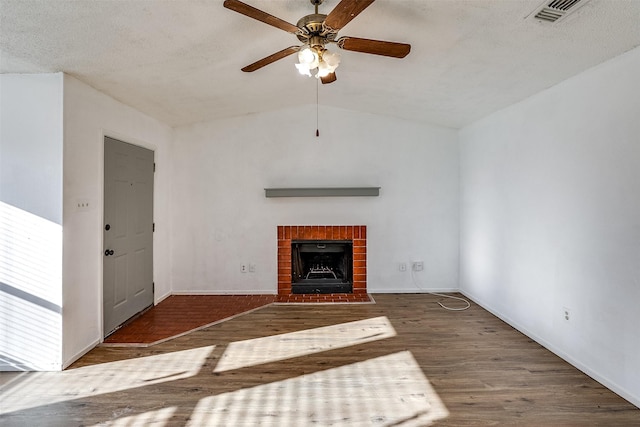 unfurnished living room featuring wood finished floors, visible vents, vaulted ceiling, a textured ceiling, and a brick fireplace