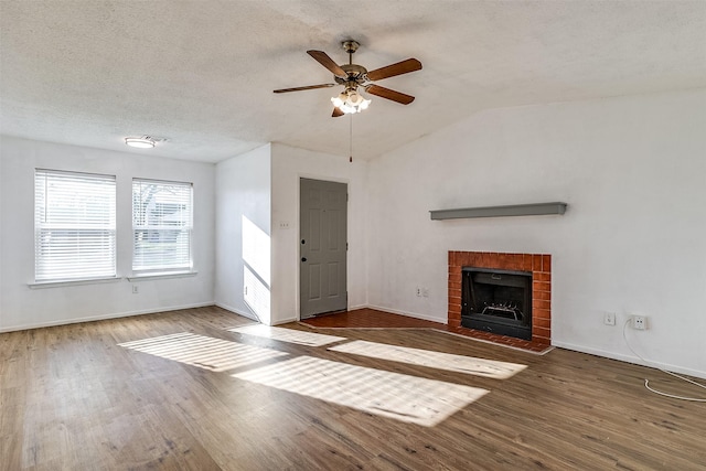 unfurnished living room featuring wood finished floors, baseboards, lofted ceiling, a fireplace, and a textured ceiling