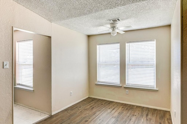 spare room with visible vents, plenty of natural light, ceiling fan, and wood finished floors