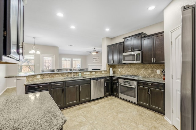 kitchen with a sink, decorative backsplash, stainless steel appliances, dark brown cabinets, and ceiling fan with notable chandelier