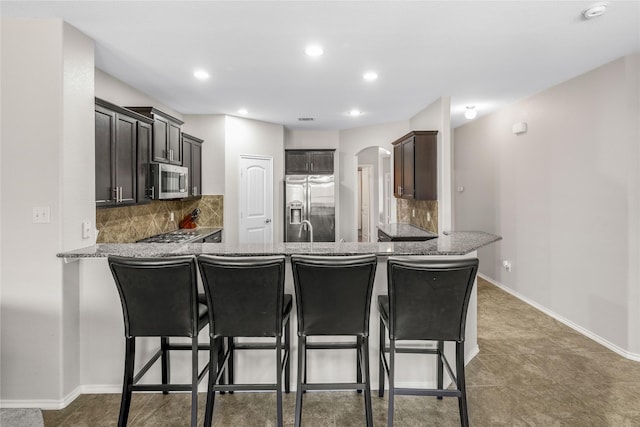 kitchen with stone countertops, stainless steel appliances, arched walkways, a peninsula, and baseboards