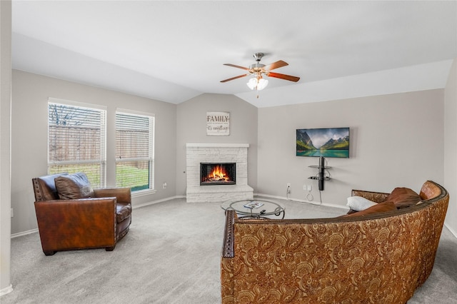 carpeted living area featuring vaulted ceiling, a ceiling fan, baseboards, and a warm lit fireplace