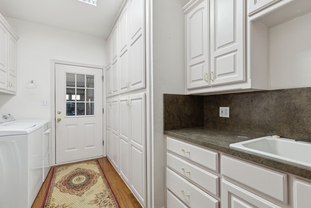 clothes washing area with washer and dryer, cabinet space, light wood-type flooring, and a sink