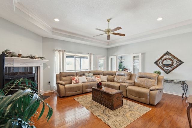 living room with a tiled fireplace, a raised ceiling, baseboards, and wood finished floors