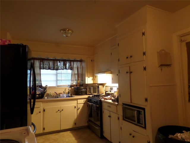 kitchen with a sink, freestanding refrigerator, gas stove, white cabinets, and light countertops