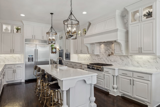 kitchen with white cabinetry, premium range hood, built in appliances, and a sink