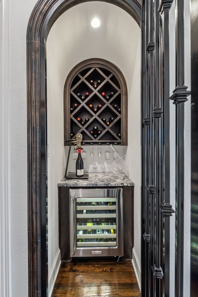 bar featuring beverage cooler, a dry bar, dark wood-type flooring, and baseboards