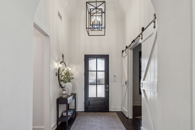 foyer entrance featuring visible vents, a barn door, a high ceiling, baseboards, and dark wood-style flooring