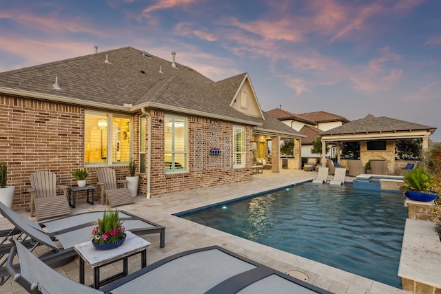 back of house featuring a patio, brick siding, a pool with connected hot tub, and a shingled roof