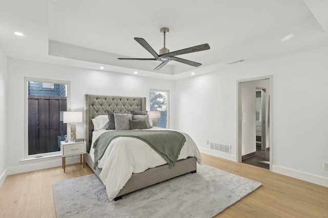 bedroom with a tray ceiling, visible vents, wood finished floors, and recessed lighting