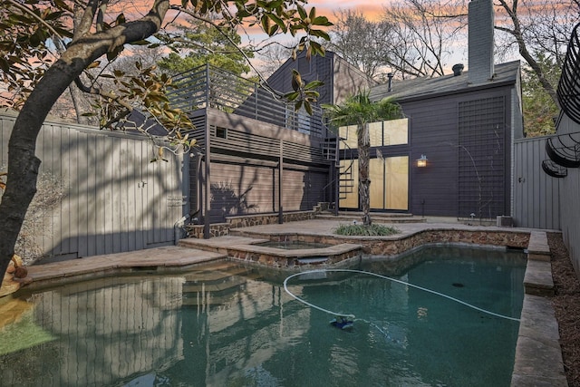 pool at dusk featuring an outdoor pool, an in ground hot tub, and a patio