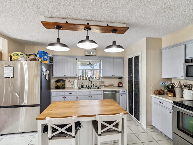 kitchen featuring light tile patterned floors, appliances with stainless steel finishes, pendant lighting, and a sink