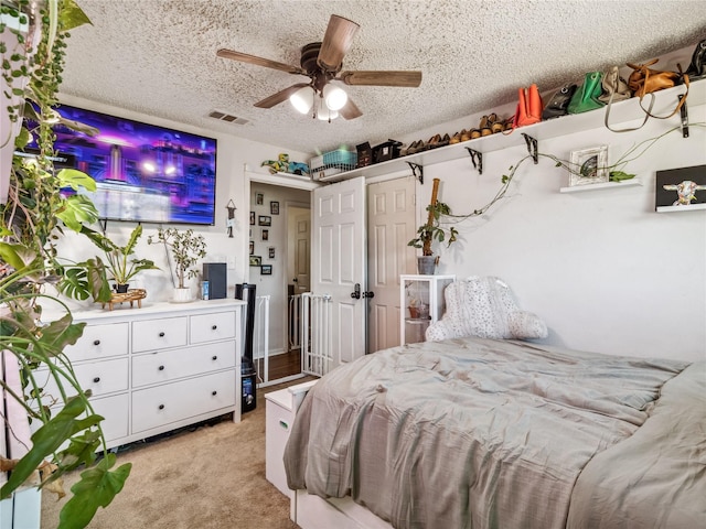 bedroom featuring visible vents, light colored carpet, a textured ceiling, and a ceiling fan