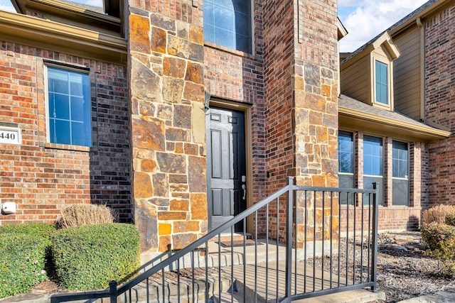 view of exterior entry with brick siding and roof with shingles