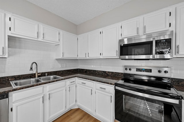 kitchen with a sink, a textured ceiling, appliances with stainless steel finishes, and white cabinetry