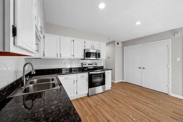 kitchen featuring visible vents, light wood-style flooring, a sink, white cabinets, and appliances with stainless steel finishes