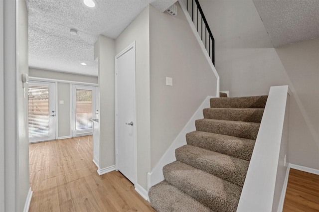 staircase featuring recessed lighting, baseboards, a textured ceiling, and wood finished floors