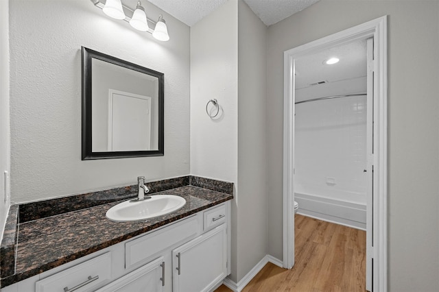 bathroom with vanity, wood finished floors, a textured ceiling, shower / bathing tub combination, and toilet