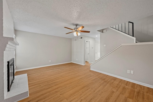 unfurnished living room with light wood-type flooring, a ceiling fan, a textured ceiling, baseboards, and a brick fireplace