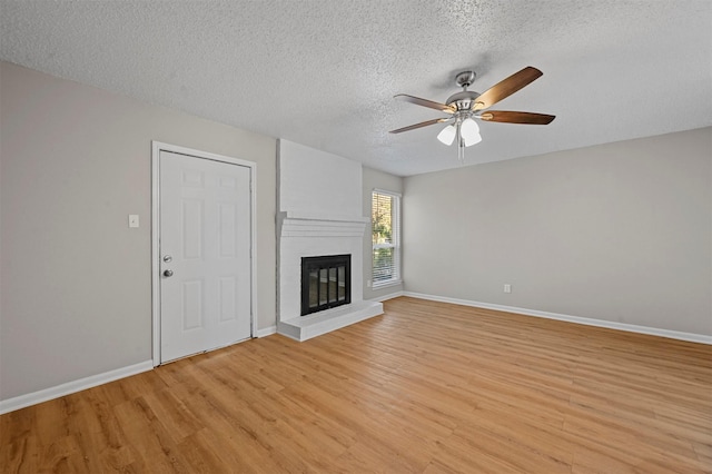 unfurnished living room featuring baseboards, light wood-style flooring, a fireplace, a textured ceiling, and a ceiling fan