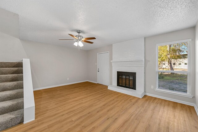 unfurnished living room featuring stairway, baseboards, a brick fireplace, and light wood finished floors