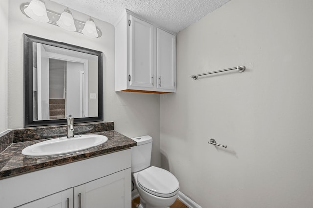 half bathroom featuring baseboards, a textured ceiling, vanity, and toilet