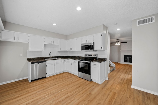 kitchen with visible vents, a brick fireplace, stainless steel appliances, white cabinetry, and a sink