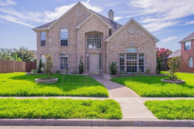 view of front of property featuring brick siding, a chimney, a front lawn, and fence