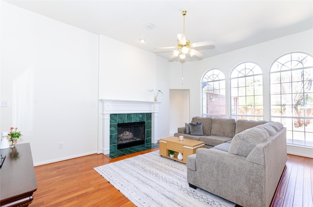 living area with visible vents, baseboards, a tile fireplace, wood finished floors, and a ceiling fan