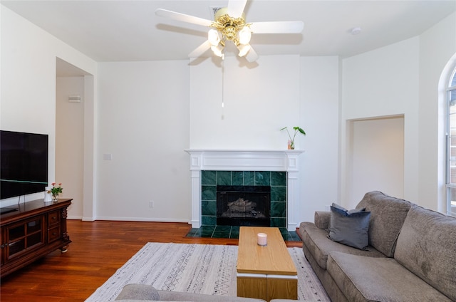 living area with baseboards, wood finished floors, a ceiling fan, and a tile fireplace