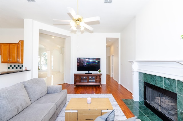 living room featuring wood finished floors, baseboards, arched walkways, ceiling fan, and a tile fireplace