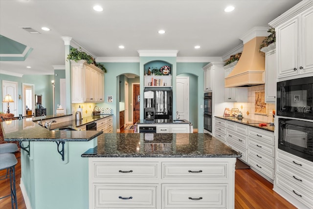 kitchen featuring visible vents, custom range hood, arched walkways, black appliances, and a sink