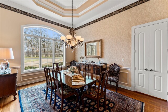 dining space with wood finished floors, an inviting chandelier, ornamental molding, and wainscoting