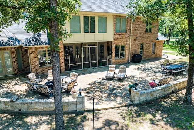 rear view of property featuring french doors, a patio, brick siding, and a sunroom