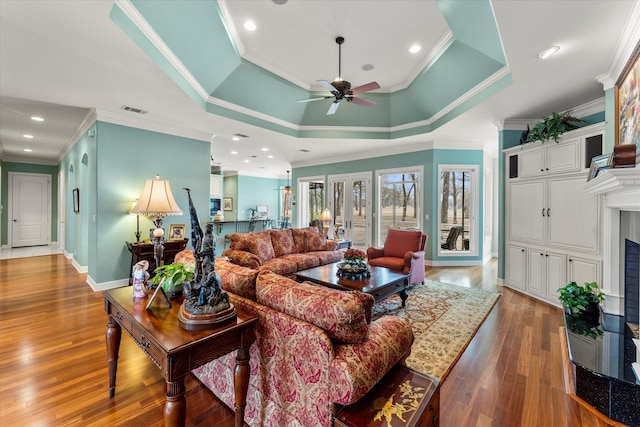 living area with a fireplace with raised hearth, baseboards, a tray ceiling, recessed lighting, and hardwood / wood-style flooring