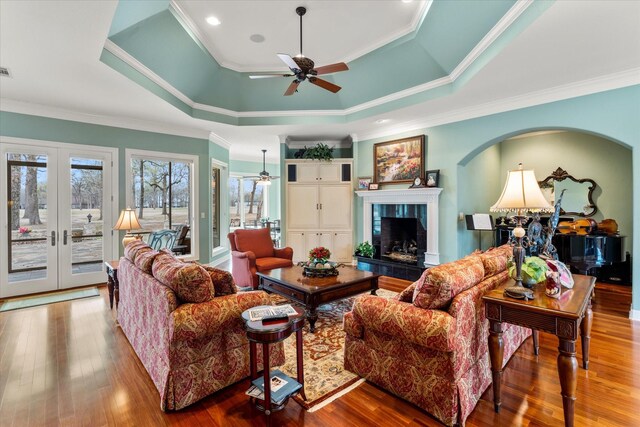 living room with a tiled fireplace, a raised ceiling, hardwood / wood-style flooring, and french doors