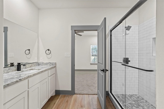 full bathroom with a stall shower, vanity, baseboards, and wood finished floors