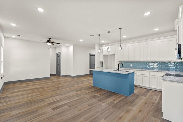 kitchen featuring light wood-type flooring, a sink, tasteful backsplash, open floor plan, and white cabinets