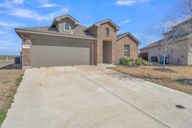 view of front of house featuring an attached garage, cooling unit, brick siding, and driveway