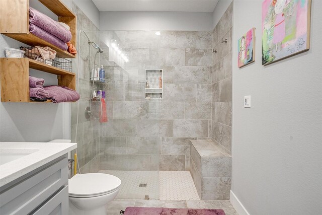 bathroom featuring toilet, tiled shower, and vanity