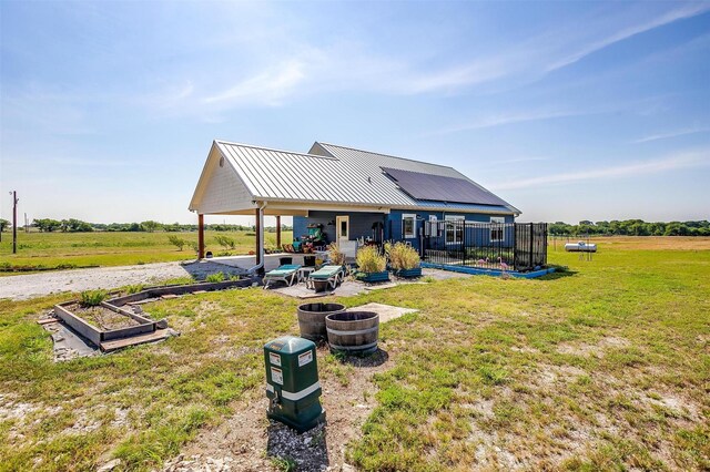 back of house featuring a lawn, a patio, roof mounted solar panels, a fire pit, and metal roof