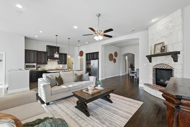 living room featuring visible vents, wood finished floors, arched walkways, a stone fireplace, and ceiling fan