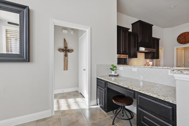 kitchen featuring light stone counters, baseboards, light tile patterned flooring, decorative backsplash, and under cabinet range hood